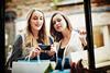 Two women looking at products in a shop window and taking a photo with their phone